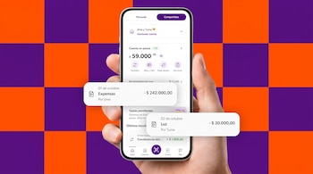 Mano que sostiene un teléfono móvil con una aplicación de finanzas sobre un fondo a cuadros naranja y violeta