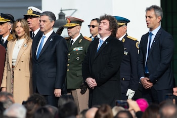 Vista frontal de Javier Milei en abrigo negro y Fátima Flórez en abrigo beige, junto a funcionarios y militares, de pie al aire libre durante una ceremonia