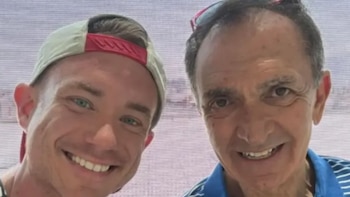 Un hombre mayor sonriente con polo azul y gafas de sol en la cabeza (Dean Trantalis), junto a un hombre más joven con gorra de béisbol y ojos azules brillantes