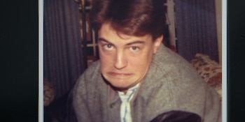 Fotografía en plano medio del joven Matthew Perry mirando al frente con los labios apretados hacia abajo, vestido con chaqueta gris y corbata