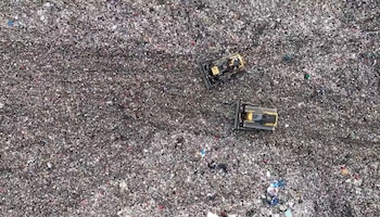 Vista aérea de dos bulldozers amarillos sobre un extenso campo de residuos que contiene basura, plástico y escombros