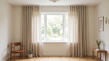 Ventana central con cortinas beige abiertas hasta el suelo, una silla de madera, una planta pequeña y una mesa auxiliar.