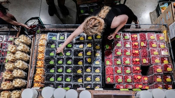 Vista aérea de una persona en un supermercado seleccionando una caja de moras de un expositor refrigerado lleno de frutas y queso preenvasados