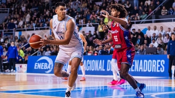 Un baloncestista con uniforme blanco de Argentina sostiene el balón mientras un rival con uniforme rojo de Puerto Rico intenta defender