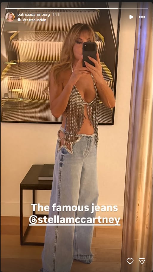 Patricia Della Giovampaola posa frente a un espejo con un top de flecos brillantes y un pantalón de mezclilla de corte amplio con aberturas laterales.