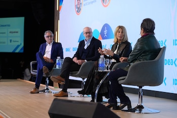 Cuatro personas sentadas en sillones individuales sobre un escenario conversan frente a una pantalla con la marca IDEA