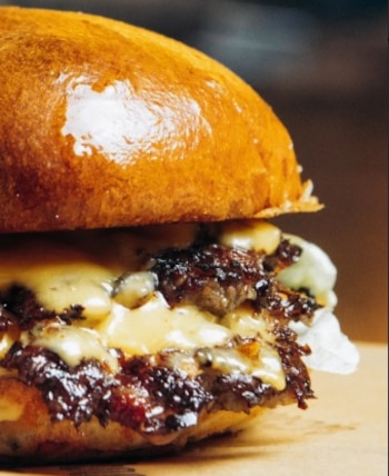 Doble smash de carne madurada, cheddar, lechuga y cebolla en pan de papa, con protagonismo de la carne y el queso