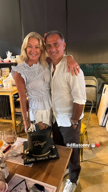Diego Latorre y Yanina Latorre abrazados junto a una torta negra con los textos "Diego" y "Feliz Cumple Papá", decorada con dos figuras de perros