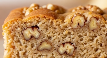 Primer plano de un corte de budín de color marrón claro con trozos grandes de nueces incrustados en su miga.