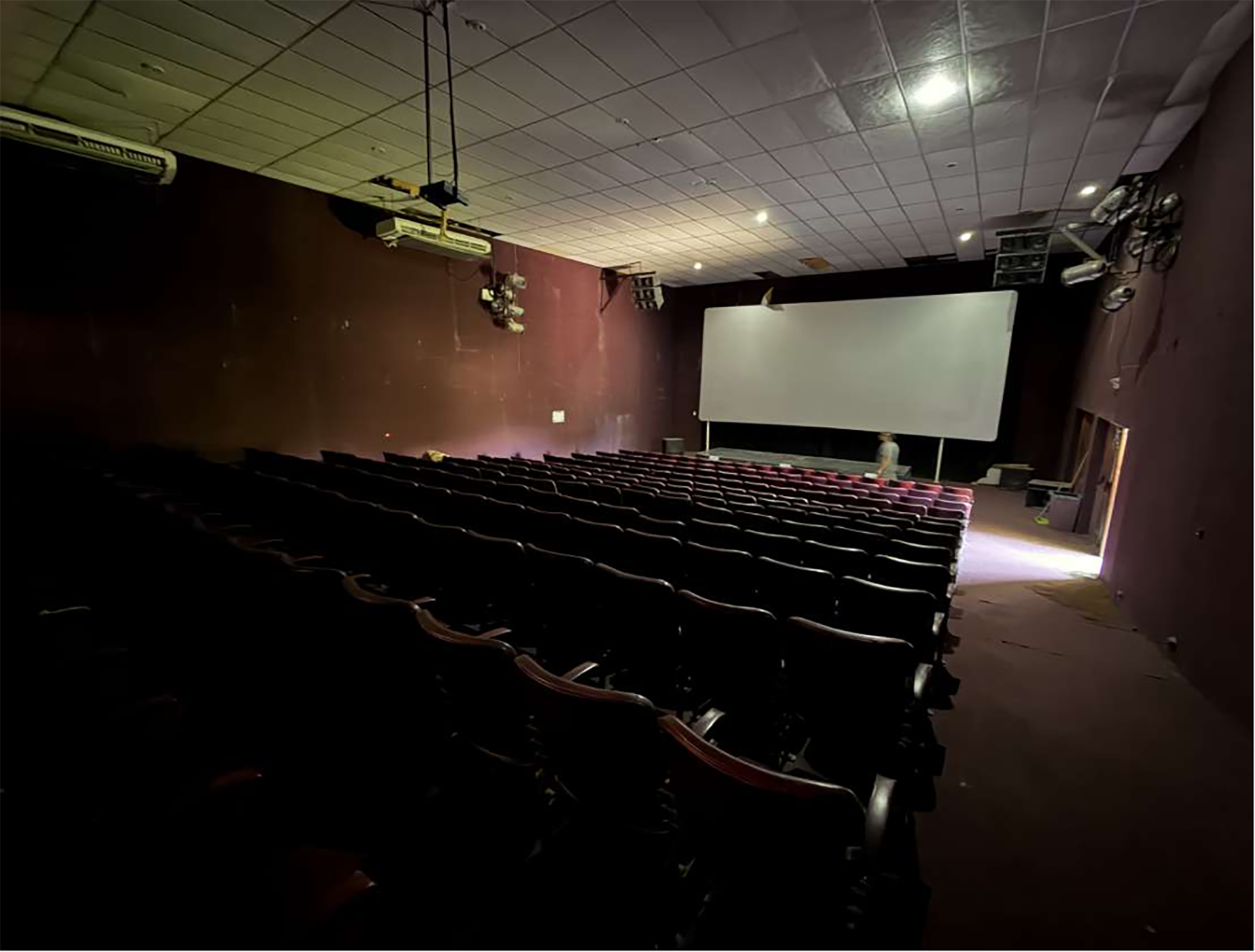 El interior de un centro de artes escénicas, con filas de asientos vacíos y una pantalla grande, muestra la quietud del lugar esperando futuros eventos o su rehabilitación.