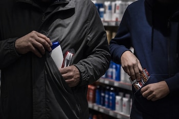 Manos de dos personas guardando un champú, cepillos de dientes y alimentos en los bolsillos de sus abrigos.