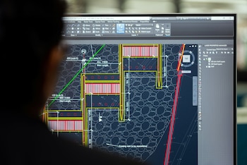 Una persona observa una pantalla de ordenador que muestra el software Autodesk AutoCAD Civil 3D con un plano técnico, líneas, texto y dimensiones