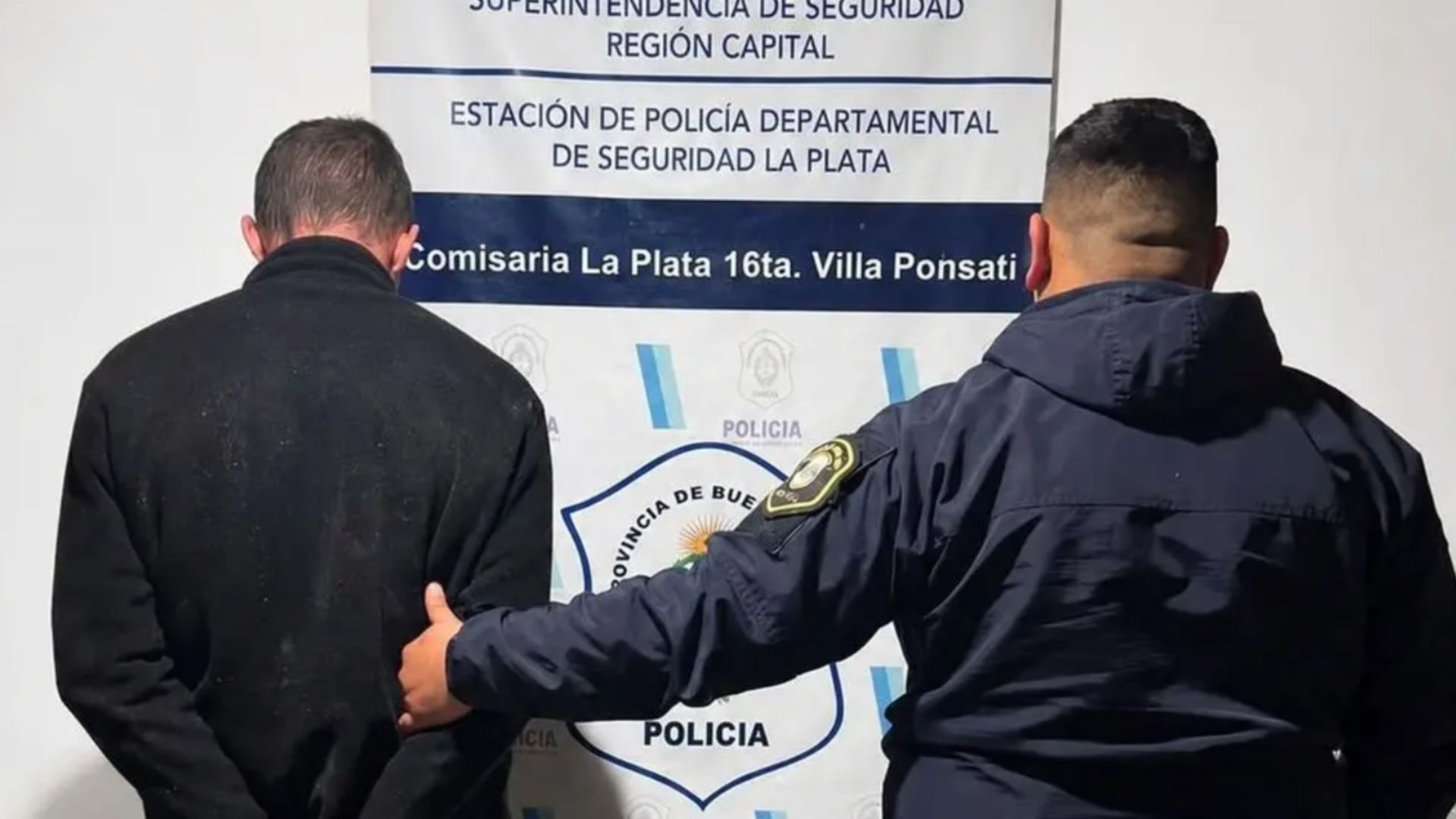 Un hombre es retenido por un agente de policía frente al cartel de la Comisaría La Plata 16ta. Villa Ponsati, tras ser detenido por robo (La Buena Info)