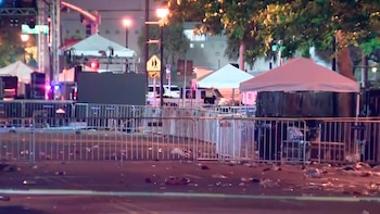 Vista nocturna de una calle con barricadas metálicas, carpas blancas temporales y basura esparcida en el suelo. Luces de vehículos policiales son visibles al fondo
