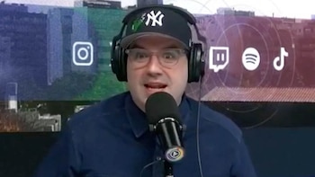 Hombre con gorra negra de los New York Yankees, gafas y auriculares, hablando por un micrófono. Detrás, una pantalla muestra logos de Instagram, Twitch, Spotify y TikTok
