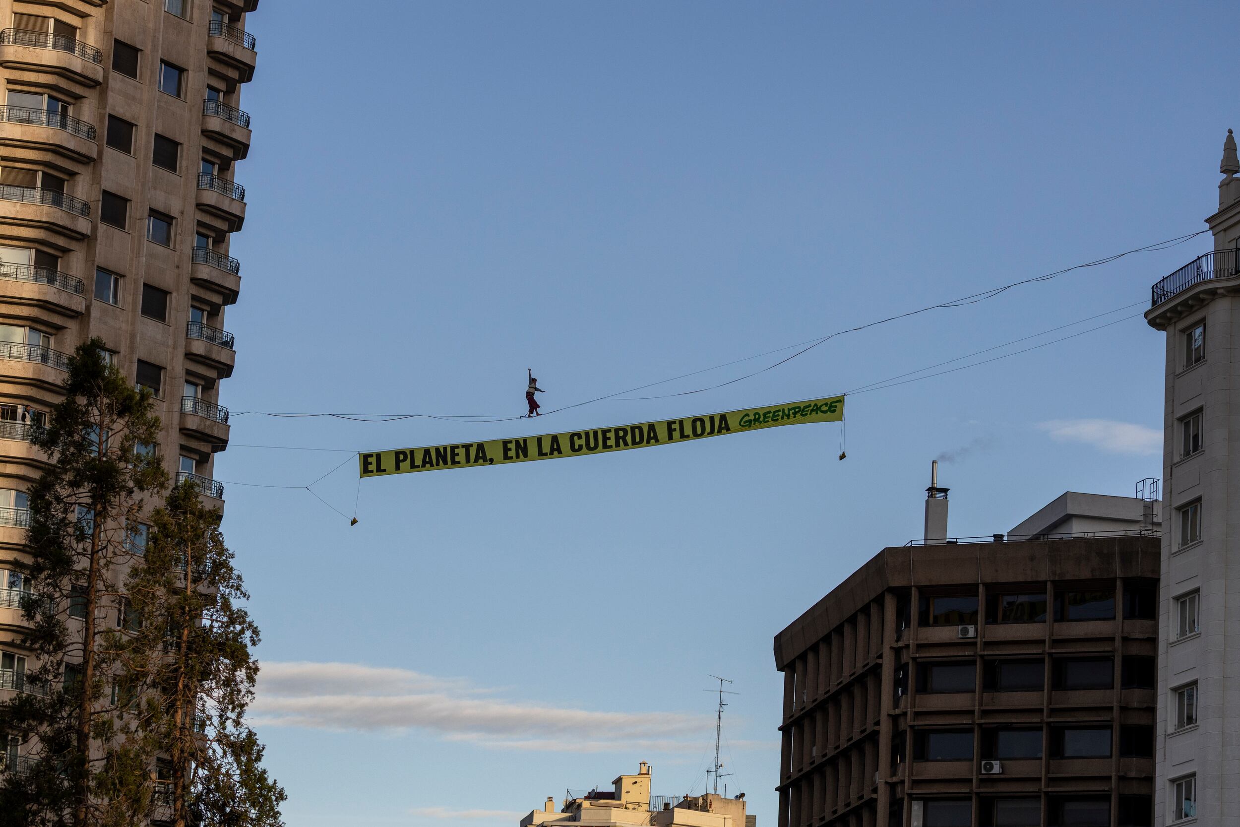 Una activista de Greenpeace camina a 30 metros de altura sobre la calle Princesa de Madrid para denunciar que la COP30 arranca con “el planeta en la cuerda floja”
