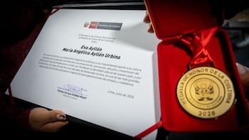 Una mano sostiene un certificado blanco con el logo del Ministerio de Cultura de Perú; otra mano sujeta una caja roja de terciopelo que contiene una medalla dorada