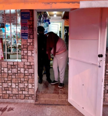 Un agente con uniforme oscuro custodia a una persona que se cubre la cara con un abrigo en la salida de un comercio