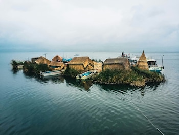 Isla de cañas sobre el agua con pequeñas chozas de paja, botes a motor y una lancha de pasajeros en un día nublado
