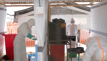 Tres personas con trajes de protección biológica blancos y mascarillas permanecen junto a depósitos de agua y contenedores de residuos
