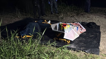 Varias personas, rescatistas con chalecos anaranjados y un agente policial junto a una lancha blanca llamada Kej en una orilla nocturna