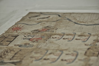 Fragmento de un lienzo antiguo con dibujos de un sol, personas a caballo, senderos azules e inscripciones escritas a mano