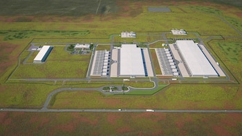 Vista aérea de un complejo industrial con cuatro grandes edificios, múltiples estructuras pequeñas, carreteras, vehículos, zonas de estacionamiento y terrenos verdes