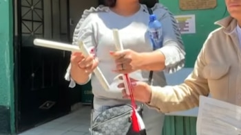 Una mujer sostiene en sus manos los fragmentos de una varilla blanca rota mientras otra persona a su lado sostiene unos papeles