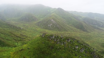 Vista aérea de colinas cubiertas de vegetación verde con rocas sobre la cima bajo un cielo con neblina