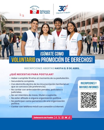 Cuatro jóvenes sonrientes, dos hombres y dos mujeres, vestidos con chalecos blancos de 'Voluntario' de la Defensoría del Pueblo, posan en un campus universitario