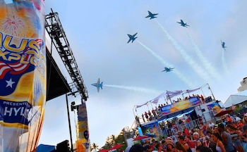 Cinco aviones a reacción azules dejan estelas de humo en un cielo claro sobre una multitud y estructuras de evento en Lummus Park, Miami