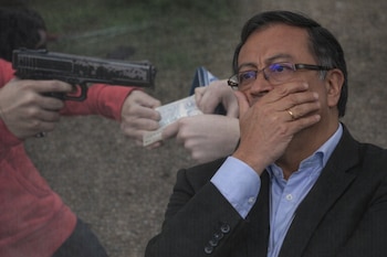 Primer plano de Gustavo Petro con traje y gafas, cubriendo su boca con la mano, sobre una imagen borrosa de una persona apuntando una pistola y manos intercambiando billetes.