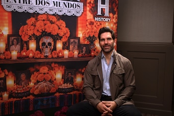 Hombre sentado ante un fondo con el logotipo de History y un altar de Día de Muertos con flores, velas y una calavera