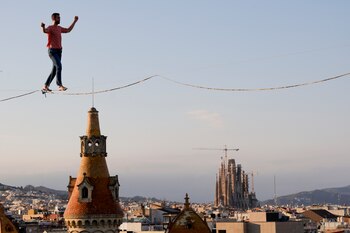 El funambulista francés Nathan Paulin recorre por un estrecho cable y en los dos sentidos los cerca de 350 metros que separan dos edificios entre la plaza Catalunya y el paseo de Gràcia, un espectáculo programado hoy domingo dentro del Grec Festival de Barcelona. EFE / Quique García.