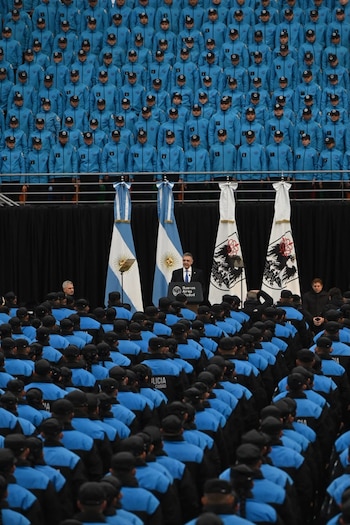 Multitud de personas uniformadas de policía. Un hombre habla en podio con texto "Buenos Aires Ciudad". Banderas argentinas y con escudos detrás