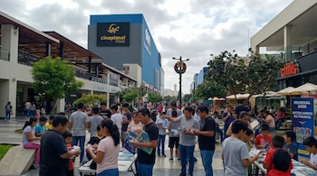 Una multitud de adultos y niños se reúne en un área peatonal al aire libre con edificios y árboles, intercambiando álbumes de figuras del Mundial 2026.