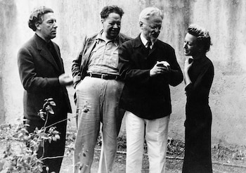 Cuatro personas, tres hombres y una mujer, posan en una foto en blanco y negro frente a una pared de fondo con vegetación en primer plano
