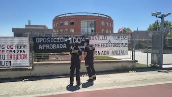Dos de los bomberos forestales junto a los carteles de protesta que han colgado en la Dirección General de Emergencias de la Comunidad de Madrid