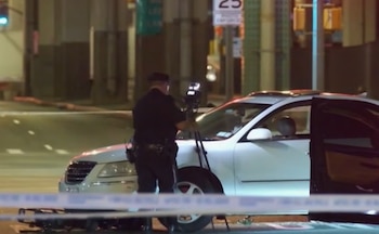 Un policía toma fotografías junto a un automóvil blanco y una bicicleta caída detrás de una cinta policial en la noche