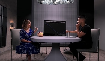 Dos personas sentadas a una mesa redonda junto a una maqueta de cerebro y un cartel con un gráfico de líneas sobre la paternidad