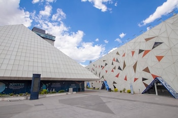 Estructura piramidal blanca y muro con patrones triangulares en una plaza al aire libre bajo un cielo azul con nubes