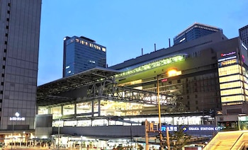 Vista exterior de Osaka Station City al anochecer, mostrando edificios modernos, estructuras metálicas y carteles luminosos bajo un cielo azul oscuro