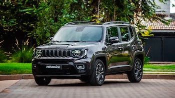 Un Jeep Renegade Serie S de color gris oscuro está estacionado en un camino de adoquines. Abundante vegetación verde y árboles se ven al fondo