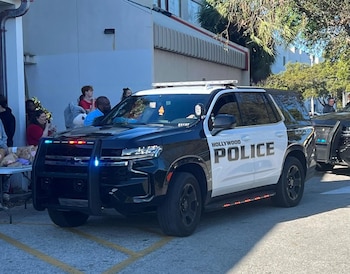 SUV policial negro y blanco con las palabras Hollywood Police en el costado. Tiene luces azules y rojas encendidas, una defensa frontal y personas al fondo