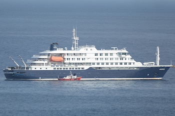 Una lancha ambulancia con tripulantes vestidos con trajes de protección se aproxima a la puerta de práctico en el costado de estribor del crucero MV Hondius, mientras permanece detenido frente al puerto de Praia, la capital de Cabo Verde, el 5 de mayo de 2026, mientras los pasajeros observan desde los puentes. (AFP)