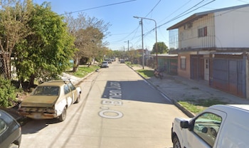 Una calle de cemento con viviendas, árboles, postes de luz, cables aéreos y automóviles estacionados a ambos lados
