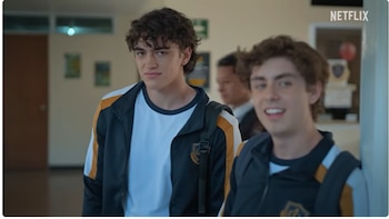 Dos hombres jóvenes en un pasillo; uno con chaqueta negra y amarilla, el otro desenfocado. El logo de Netflix aparece en la esquina superior derecha
