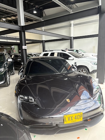 Concesionario de automóviles, un Porsche Taycan gris oscuro, varios automóviles de diferentes colores, pilares y vigas de metal, piso blanco brillante