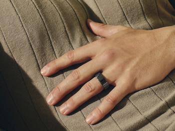 Una mano de piel oscura lleva un anillo metálico gris y sostiene el mango de una cuerda para saltar sobre un fondo de cielo azul
