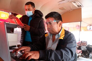 El abogado Marco Antonio Mancilla (d) recibe clientes en su autobús de transporte público, el 27 de julio de 2021, en Santa Cruz (Bolivia). EFE/ Juan Carlos Torrejón